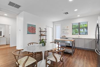 A dining room with a marble table and four chairs and a kitchen with a sink